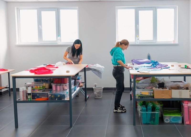 Two women working in a bright atelier, ironing and preparing fabric for fashion design