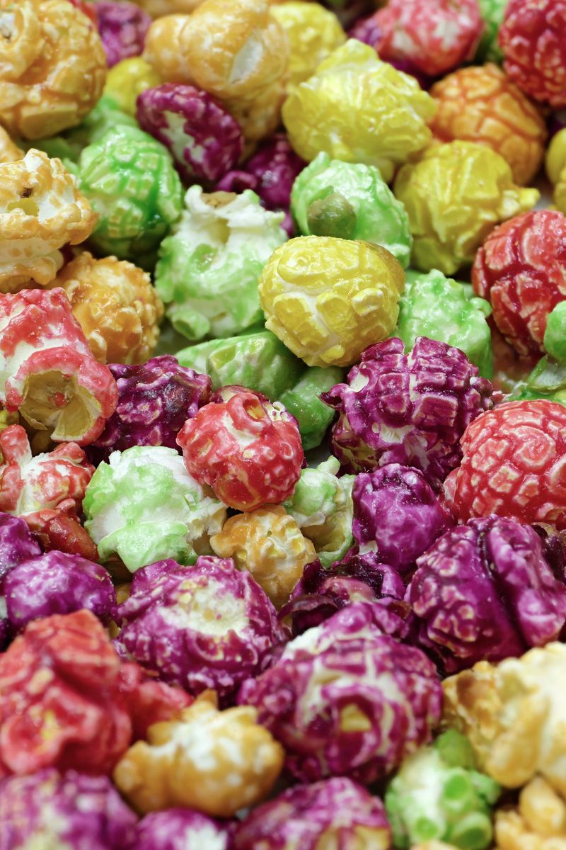 Pile of sweet popcorn coated in vibrant, multi‑colored glaze, creating a bright and eye‑catching snack display. Close-up shot, abstract food background for themes involving confectionery, desserts, snacks and sweet treats.