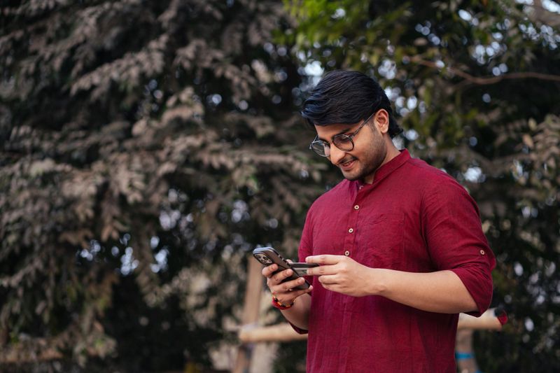 Young adult Indian man making an online payment using a mobile phone and bank card. Concept of e-commerce, fintech, digital wallet, and cashless economy.