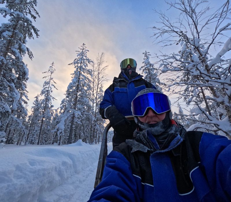 Portrait of guide and client dog sledding on trail in forest at dusk, Lapland