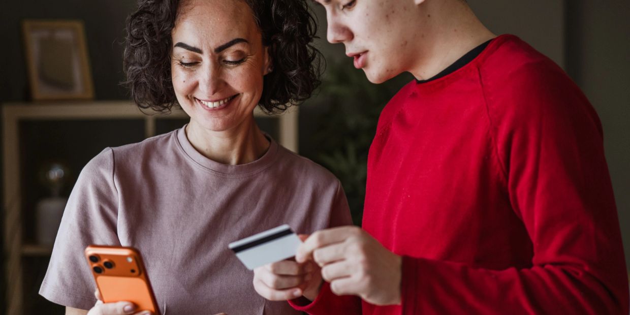 Two people using a smartphone and a credit card.