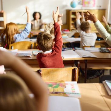 Students raising hands in classroom.