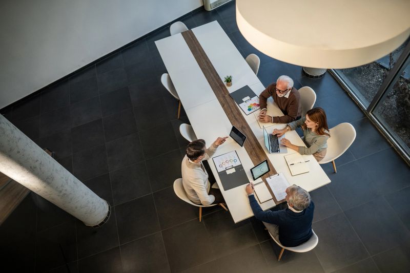 Diverse business professionals actively collaborating and discussing financial data with laptops and digital tablets on a clean meeting table in a contemporary office setting
