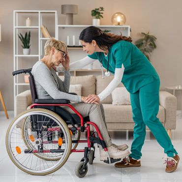 Nurse comforting a woman in a wheelchair at home.