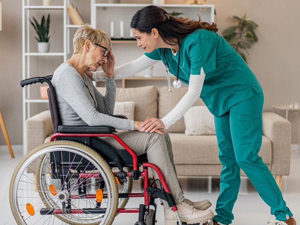 Nurse comforting elderly woman in a wheelchair at home.