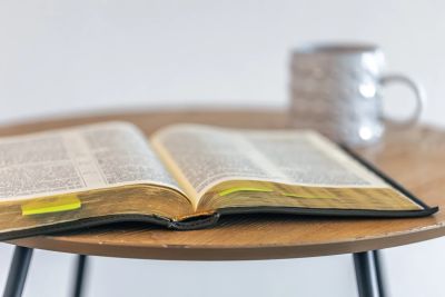 Open book on a round wooden table with a mug in the background.