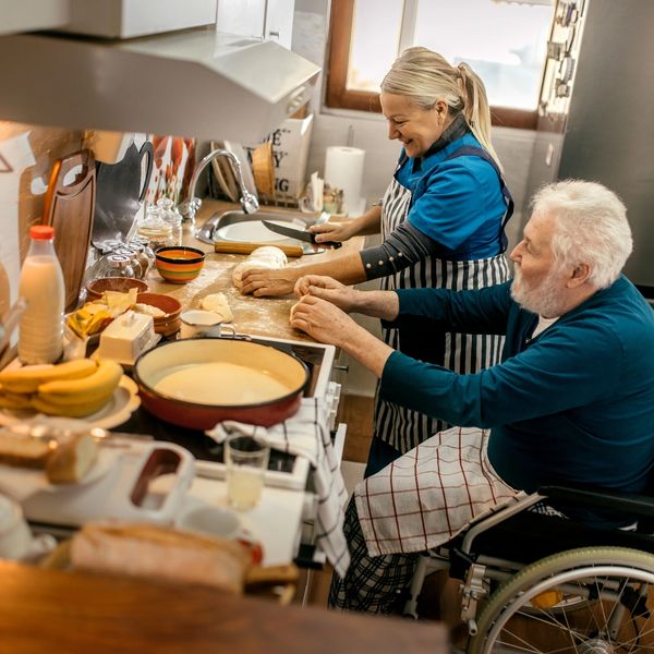An elderly man in a wheelchair and a woman cooking together.