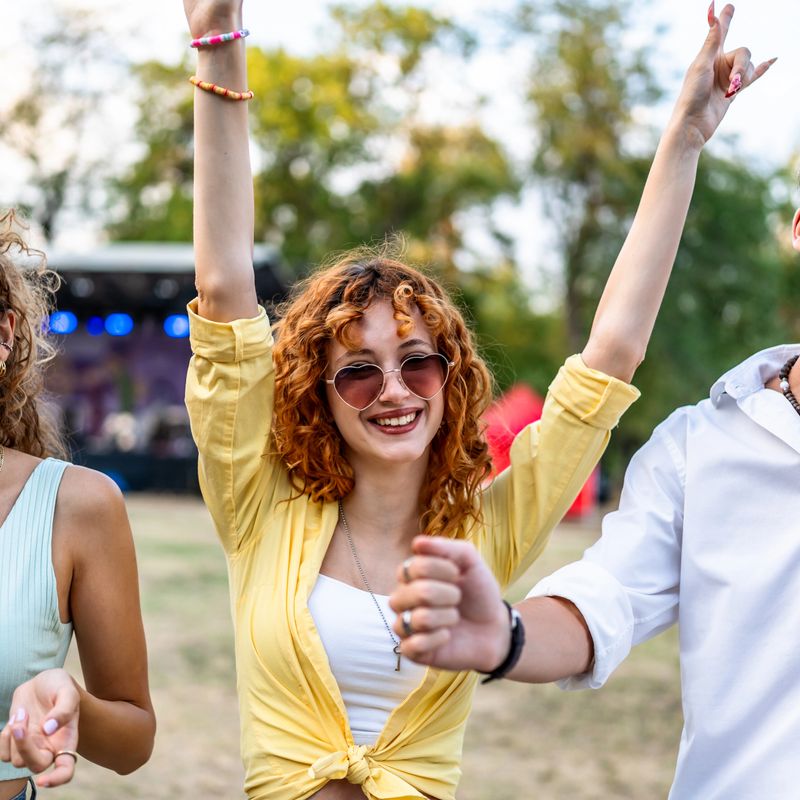 Young woman smiling and raising arms while having fun with friends at a vibrant outdoor music festival