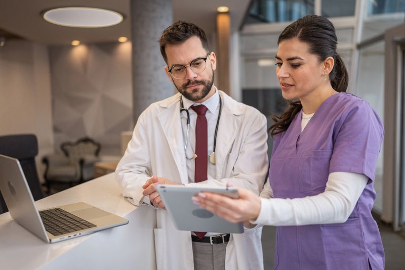 Doctor and nurse reviewing patient information on digital tablet at hospital reception