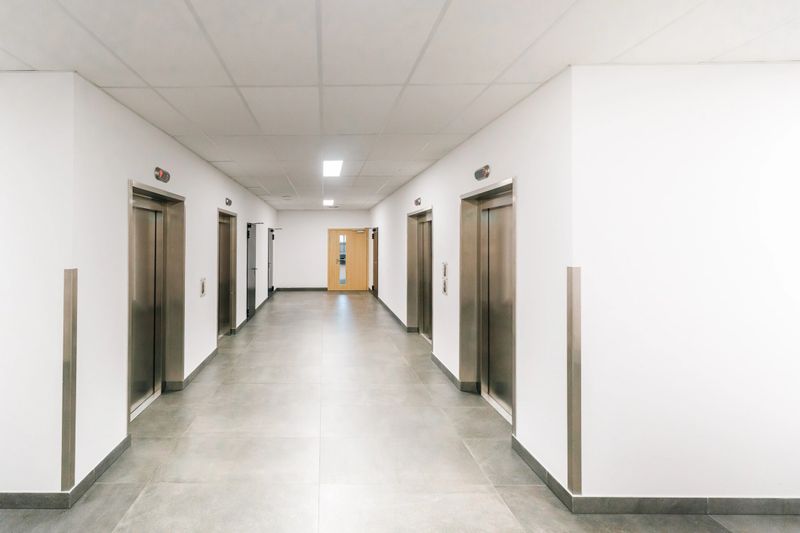 Office corridor elevators modern interior perspective. Corporate building hallway stainless steel lift doors symmetrical architecture bright lighting clean design commercial property workplace infrastructure real estate business environment