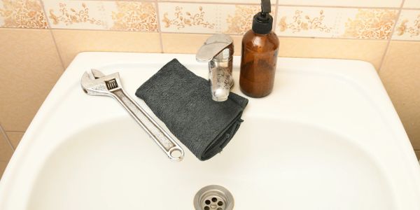 Wrench, black towel, and soap dispenser on a bathroom sink.