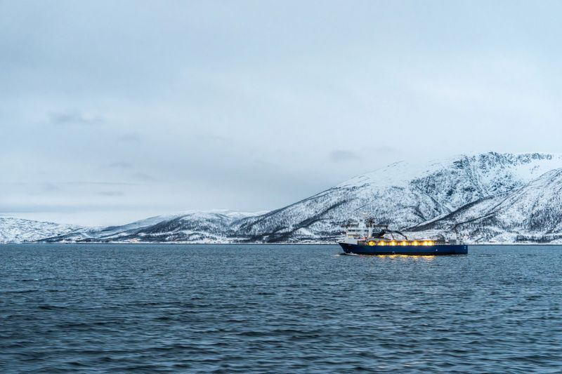 Ship sailing calm waters with snow-covered mountains in cold arctic winter