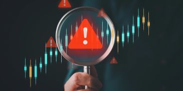 Magnifying glass highlighting a red warning symbol over a financial chart.