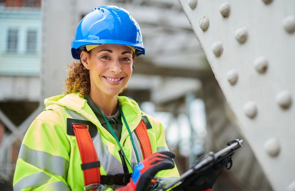Smiling female construction worker in safety gear using a tablet.