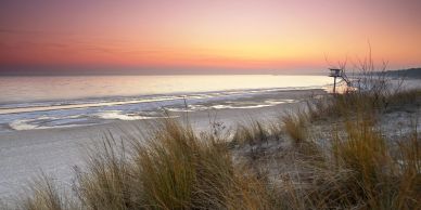 A serene beach sunset with gentle waves and dune grass in the foreground.