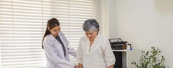 A healthcare professional assisting an elderly woman in a bright room.