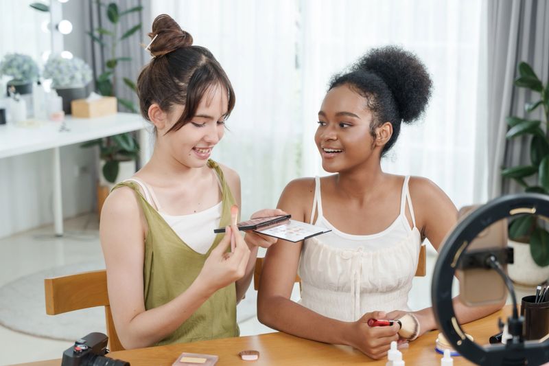 two teenage females different ethnicities recording beauty vlog using palette applying makeup smiling while filming beauty content at home studio concept youth diversity beauty influencer skincare