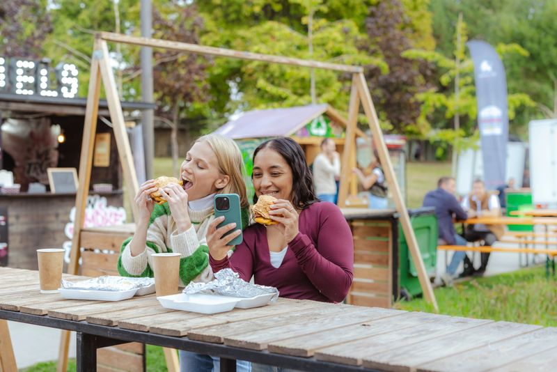 Smiling friends eating burgers and taking selfie at outdoors food festival