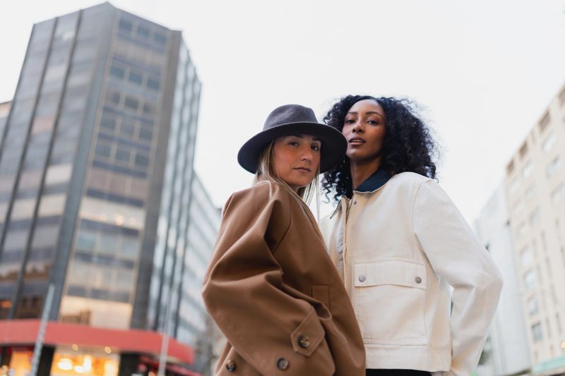 Two diverse adult women standing together in stylish outerwear with city buildings in background