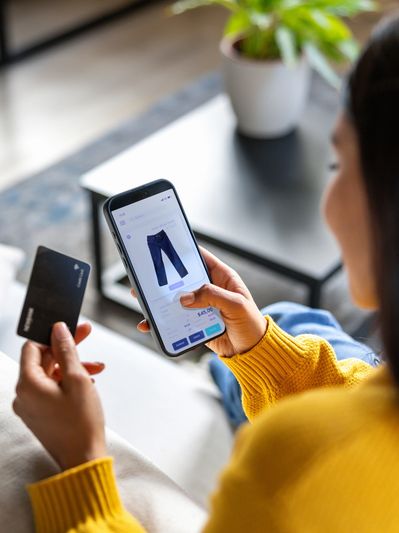 Person shopping online for pants using smartphone and credit card.