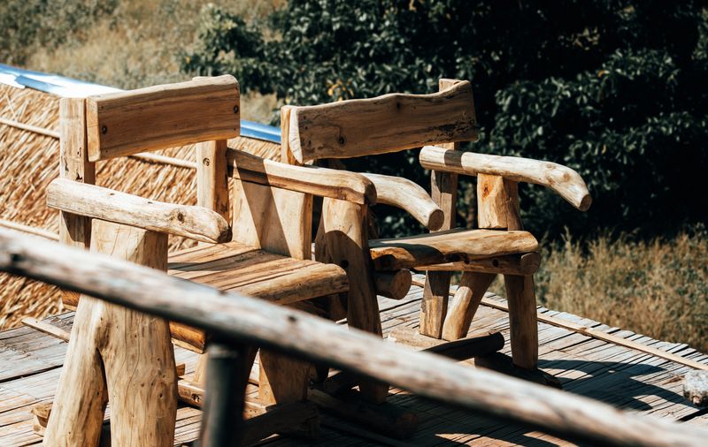 Romantic pair of rustic wooden chairs on a sunny deck, symbolic of togetherness and love in a peaceful garden, handcrafted outdoor seats for couples sharing a moment in a cozy vacation resort.