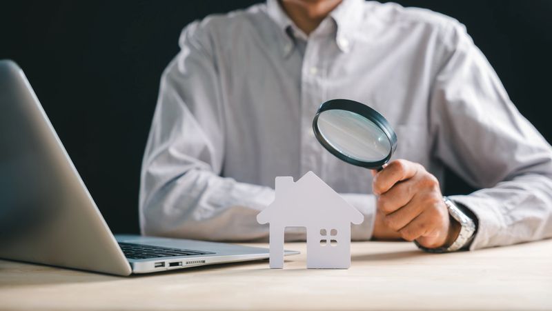 Real estate appraisal, inspector with magnifying glass on house model, searching property for home valuation, performing thorough inspection analysis using laptop technology.