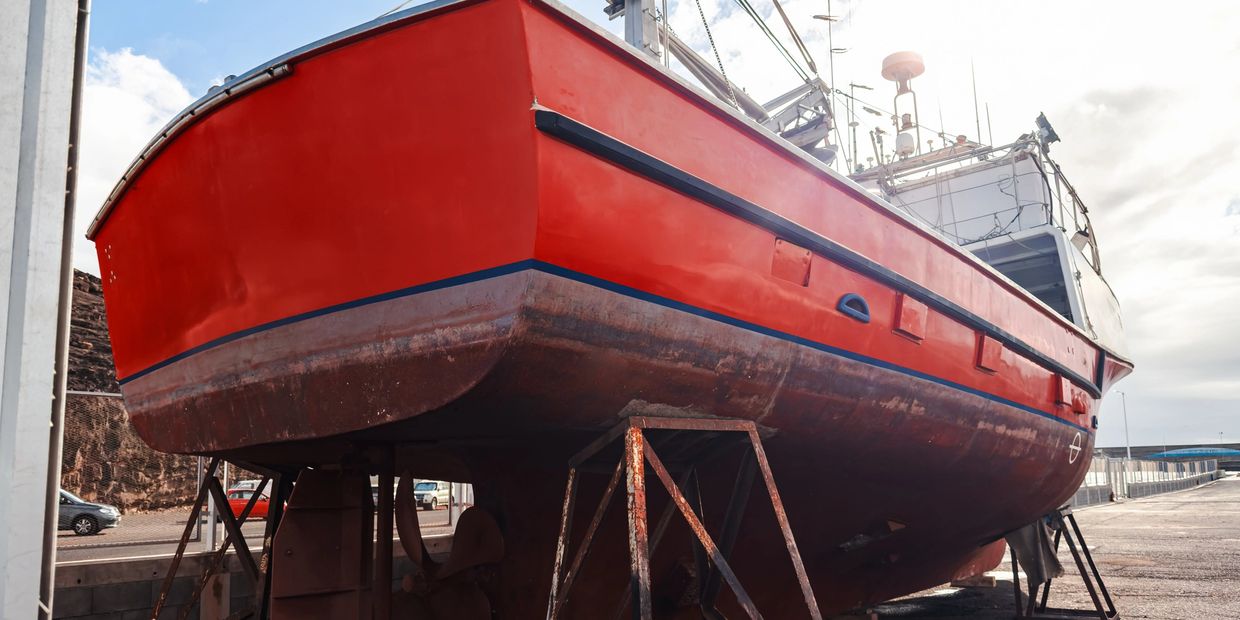 A red fishing boat on dry dock with metal supports.