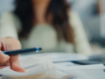 Person pointing at documents with a pen, focusing on paperwork.