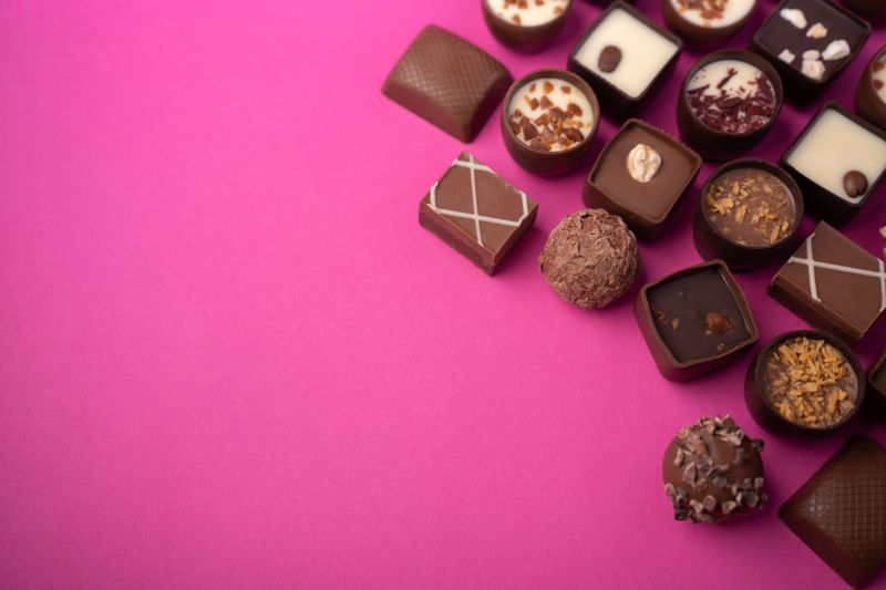 close-up flatlay of assorted gourmet chocolate bonbons and truffles on a vibrant magenta background, showcasing varied shapes, textures, nuts, creamy ganaches and glossy decorative toppings