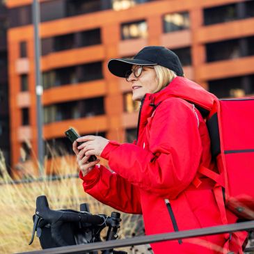 Delivery person in red jacket with bike and phone.