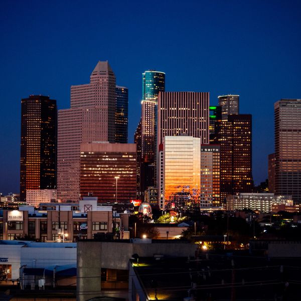 City skyline at dusk with illuminated skyscrapers and a deep blue sky.