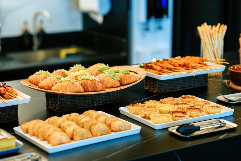 Selection of croissants, savory pastries, skewers, and baked tarts arranged on serving platters over a contemporary buffet counter in an upscale interior setting