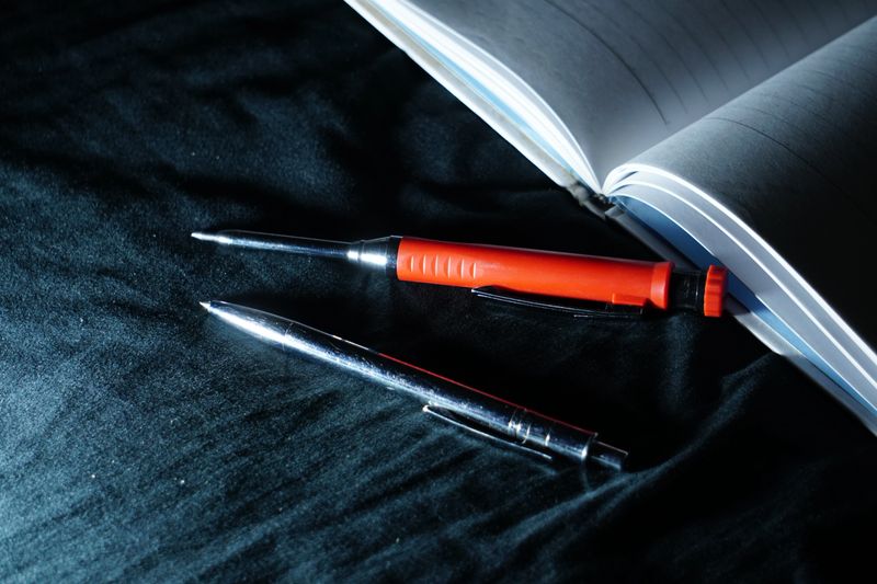 Writing tools rest on a notebook under a sharp, cool blue light, creating a focused and high-contrast atmosphere for late-night projects.