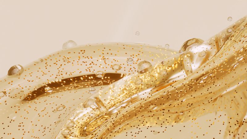 Close-up of a flowing golden liquid splash with suspended bubbles and shimmering particles against a soft neutral background. Elegant abstract concept suitable for beauty, skincare, cosmetic serum, oil, wellness, luxury branding, or premium product advertising concepts.