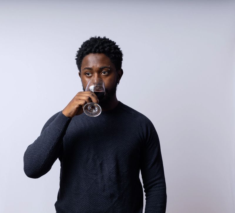 A handsome, intelligent Black Brazilian man is drinking wine against a neutral white background.