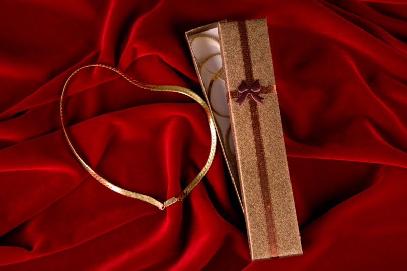 Elegant gift box with gold necklace and copy space on red velvet background