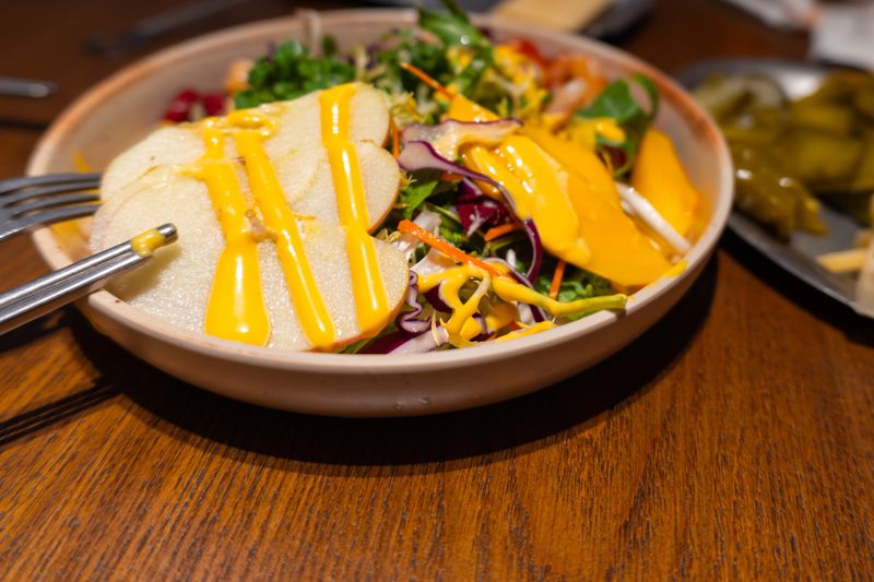 Fresh salad with sliced apples, mango, and yellow dressing on wooden table