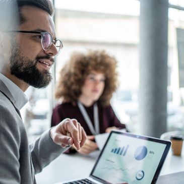 Man discussing data on laptop during meeting with colleague.