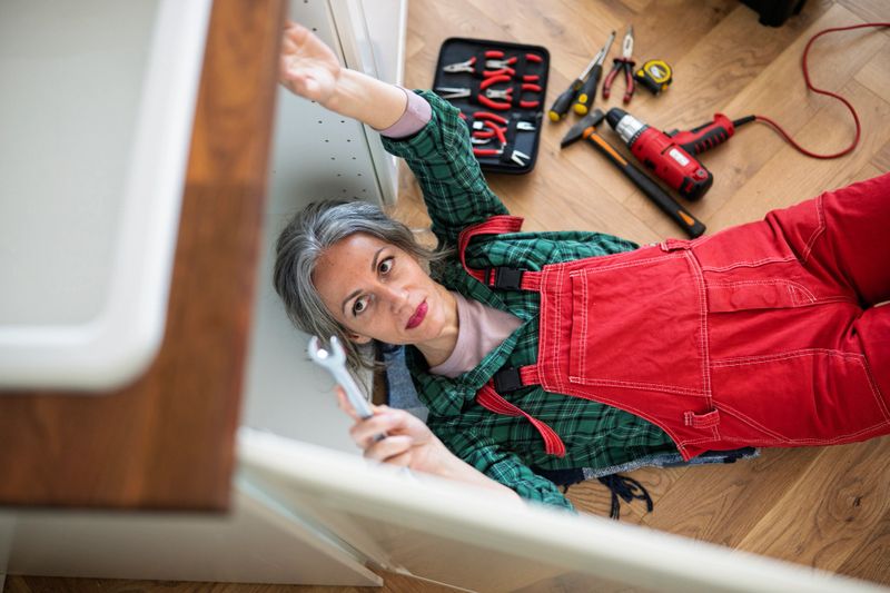 High angle shot of a mature female plumber fixing up the kitchen sink drain with plumbing tools.