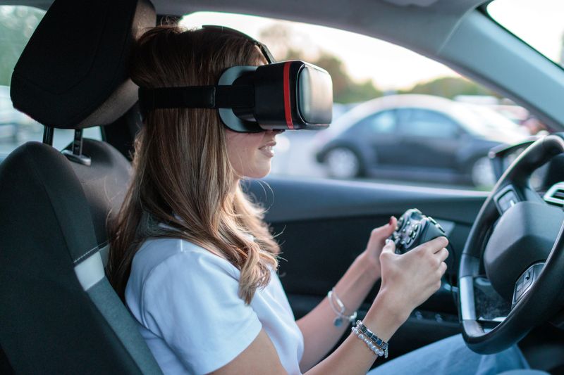 Young woman uses virtual reality glasses and a gaming controller while seated in a self-driving car