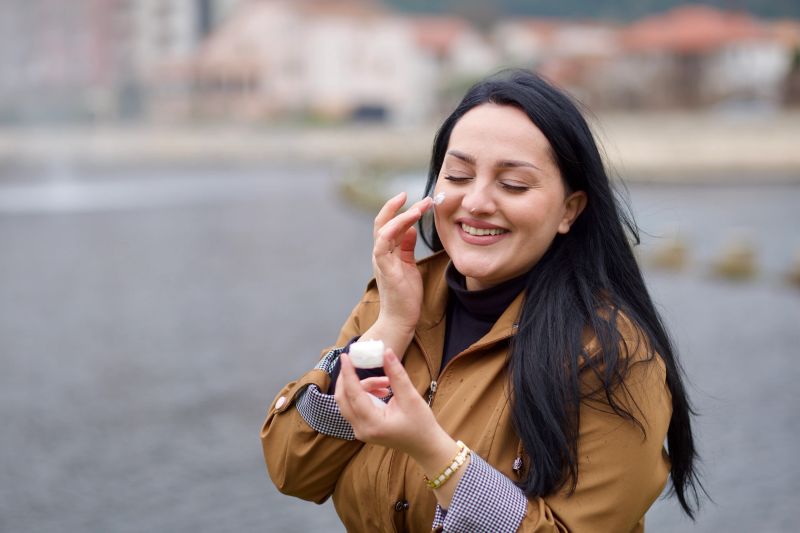 Woman applying face cream while enjoying a calm skincare routine outdoors in natural light.