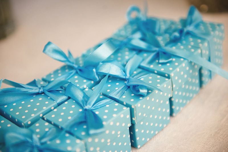 Horizontal image of small blue gift boxes with white dots and satin ribbons arranged in a neat row on light table surface. Bright blue color creates a festive celebration atmosphere.