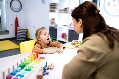 Child expressing surprise while talking to woman at table.