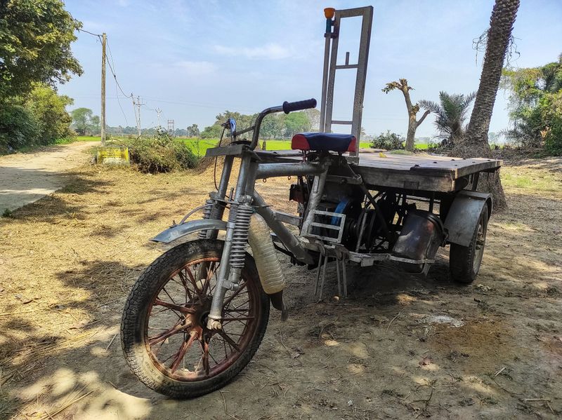 A rustic three-wheeler cargo motorcycle is parked in a rural Indian landscape, used for transporting goods and crops in villages. Highlights the sustainable transport and lifestyle in the rural area.