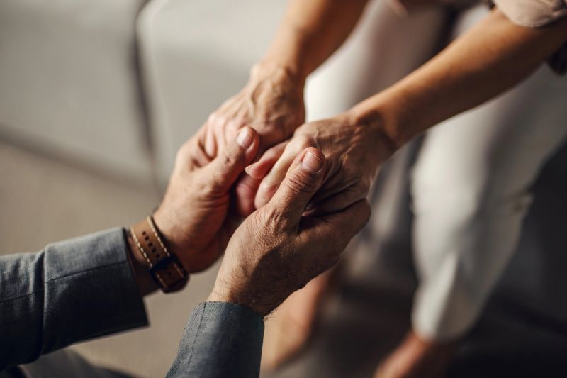 Mature adult male and female hands gently clasped together, symbolizing care, empathy, comfort, and emotional connection during a moment of profound support and trust