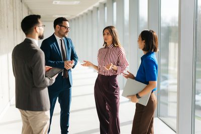 Four professionals having a discussion in a bright office corridor.