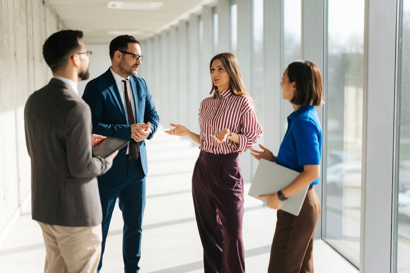Four diverse business professionals collaborating, communicating, and discussing ideas in a bright office corridor