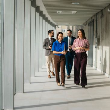 Four professionals walking and chatting in a modern office corridor.
