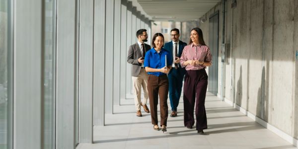 Four colleagues walking and talking in a modern office hallway.