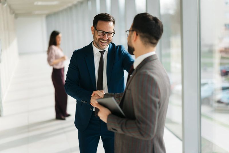 Businessmen shaking hands in a modern office hallway, completing a successful deal